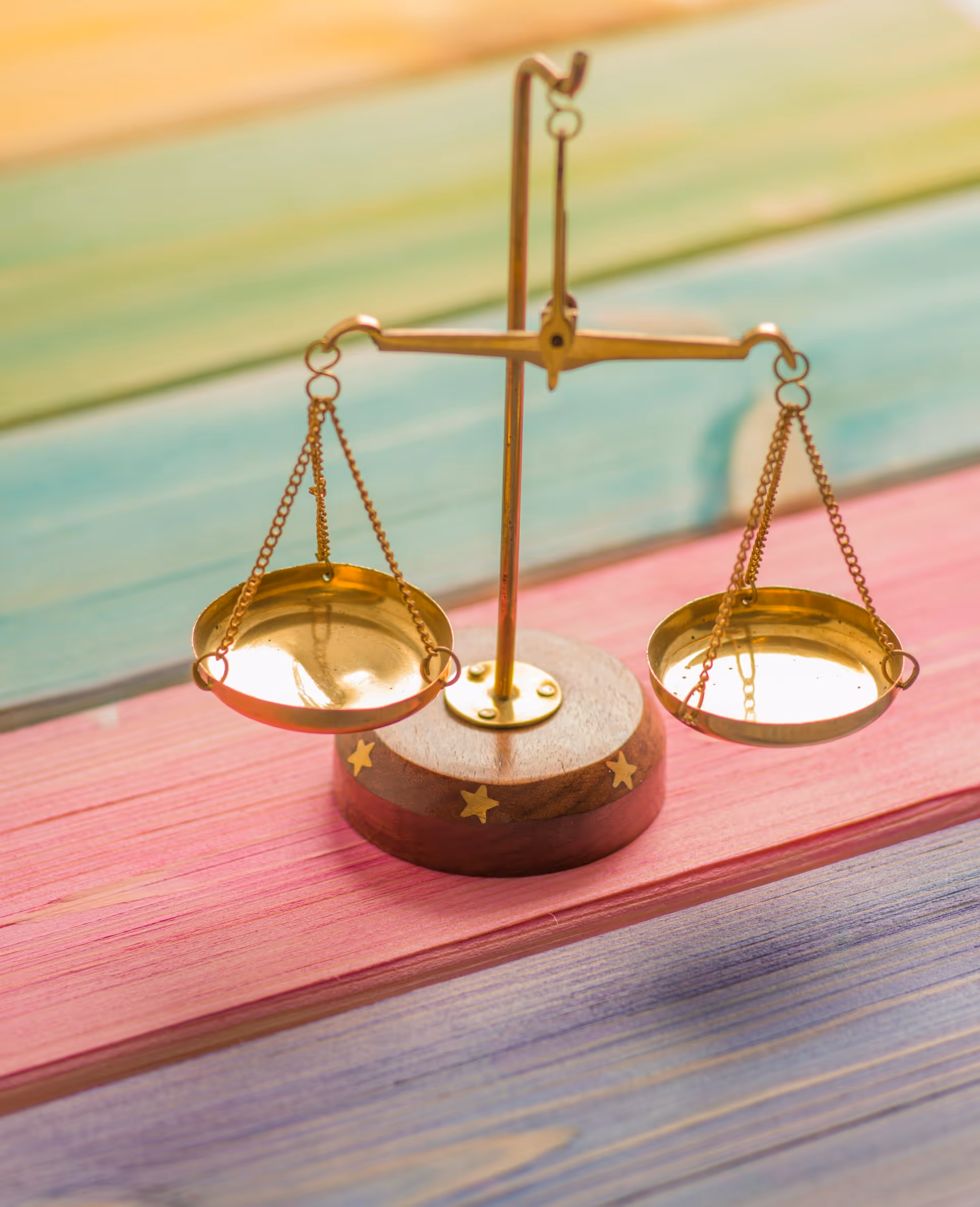 A small, gold-colored balance scale with two hanging pans placed on a colorful wooden surface