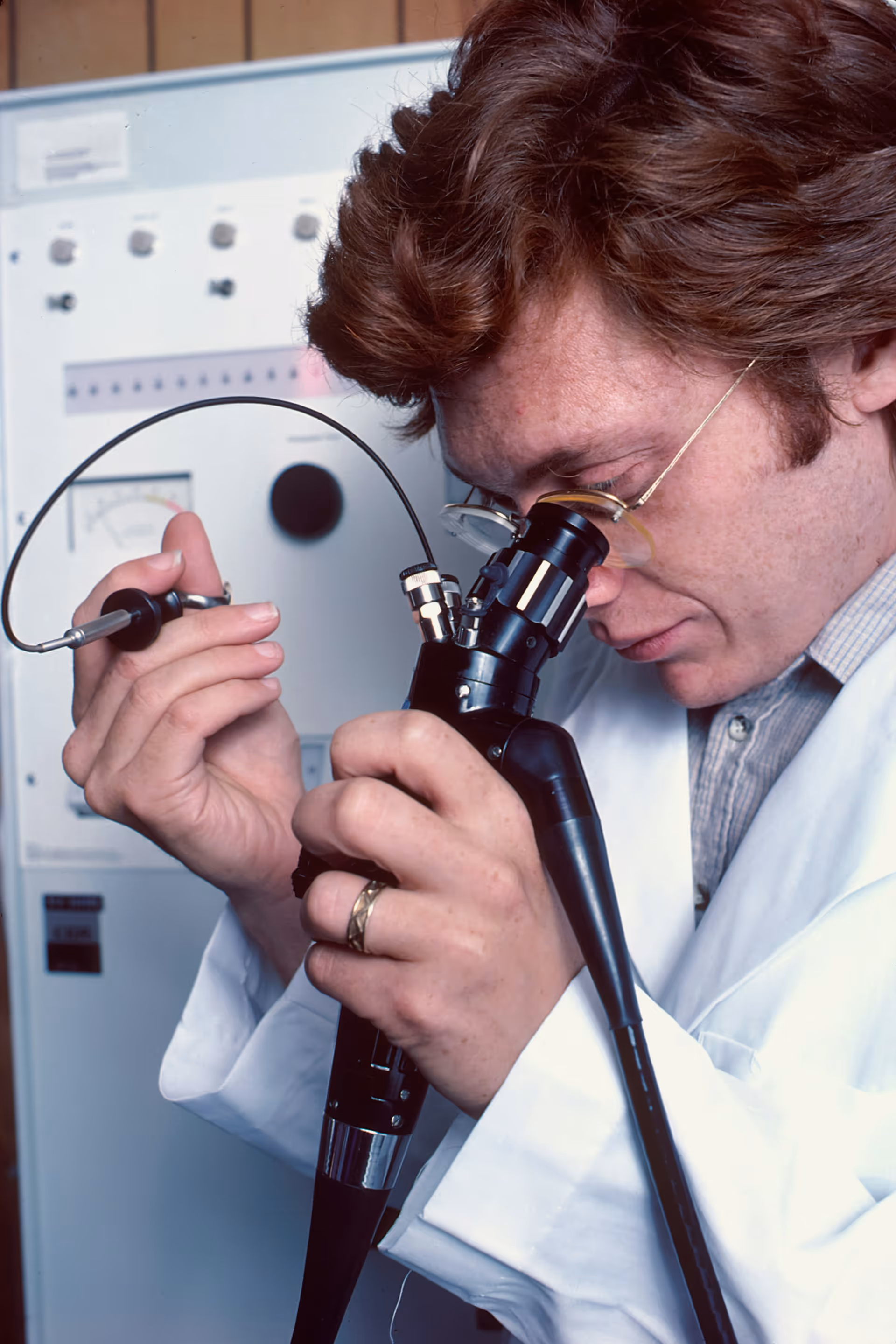 A Caucasian male physician using a remotely controlled endoscope. He is looking through a microscope-like eyepiece to monitor his actions while using small brushes and knives to take a biopsy.