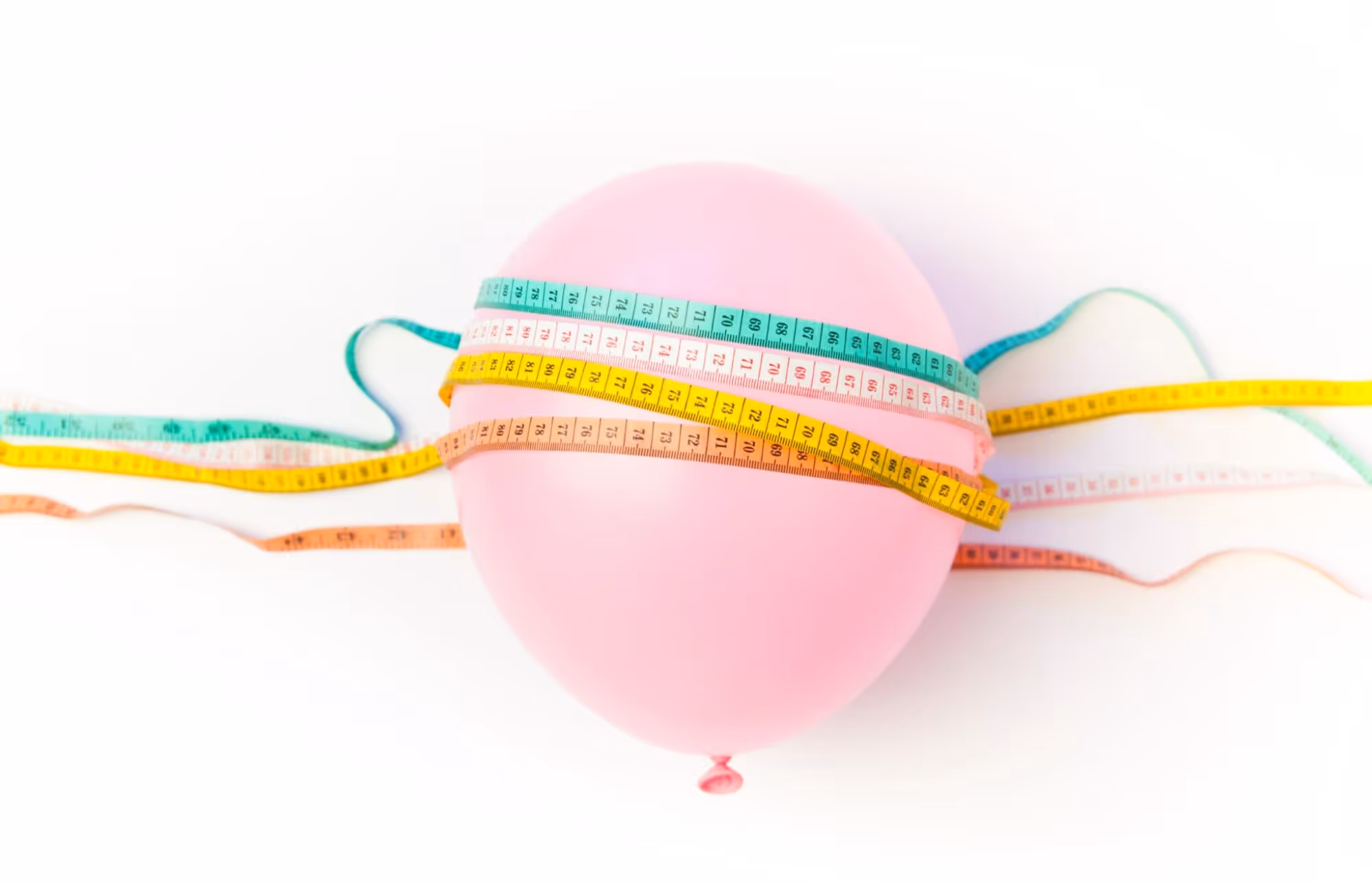 A pink balloon wrapped with multiple measuring tapes, symbolizing weight loss and measurement.