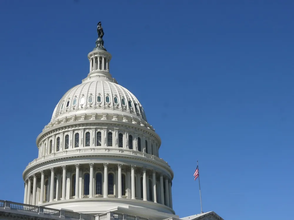 Image of the United States Capitol building with its iconic white dome and neoclassical columns set against a clear blue sky