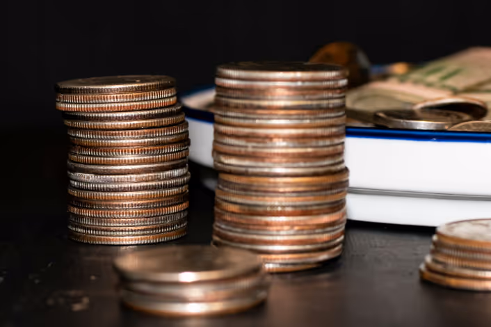 Dos pilas de monedas de veinticinco centavos frente a un plato azul y blanco