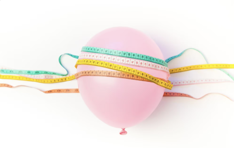 Un globo rosa envuelto con múltiples cintas métricas, simbolizando la pérdida de peso y la medición.