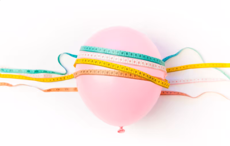 Un globo rosa envuelto con múltiples cintas métricas, simbolizando la pérdida de peso y la medición.